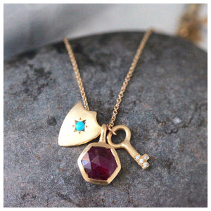Our Allegra charm necklace features 3 charms a Ruby Hexagon for balance and love, a diamond key for affection and a Shield pendant with a turquoise center stone for protection.