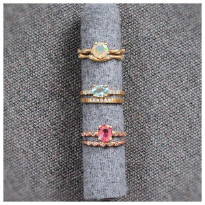 14K yellow gold stella ring with oval aquamarine center stone and 3 pave set diamonds on either side paired with our stella diamond band on a fabric roll with other rings