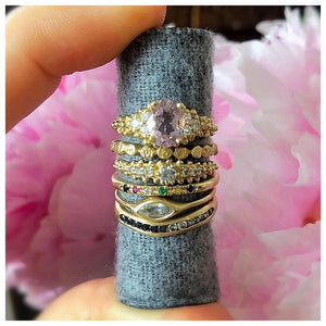 Haley ring in 14K Yellow gold with white sapphire center stone shown with other rings stacked on fabric