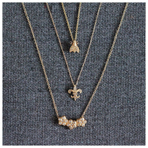 Bee necklace in 14K yellow gold with 3 white round diamonds in each wing shown with other necklaces