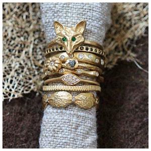 Fox Ring with Emeralds for eyes in 14K Yellow gold. Shown with other rings on rolled fabric.