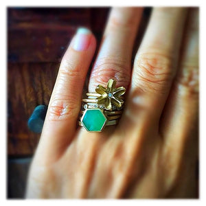 Hexagon center stone ring shown in 14K yellow gold with emerald hexagon shaped center stone. Shown worn on hand with other rings.