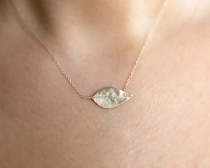 This leaf necklace features a horizontal hanging leaf shown in 14K yellow gold shown on neck.