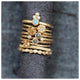 Ines ring with round opal center stone and 3 diamonds on top in 14K yellow gold showed stacked on fabric roll with other rings