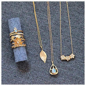 Ines ring with round opal center stone and 3 diamonds on top in 14K yellow gold shown stacked on fabric roll with various rings and necklaces