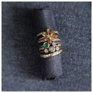 Our Molly flower bud ring in 14K yellow gold with white round diamond center stone shown stacked on fabric roll with other rings