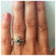 Olivia ring with green emerald center stone and white diamonds on side top and bottom shown on hand