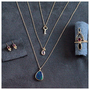 Our opal bezel pendant in 14K yellow gold with dark blue opal shown with other jewelry all sold separately